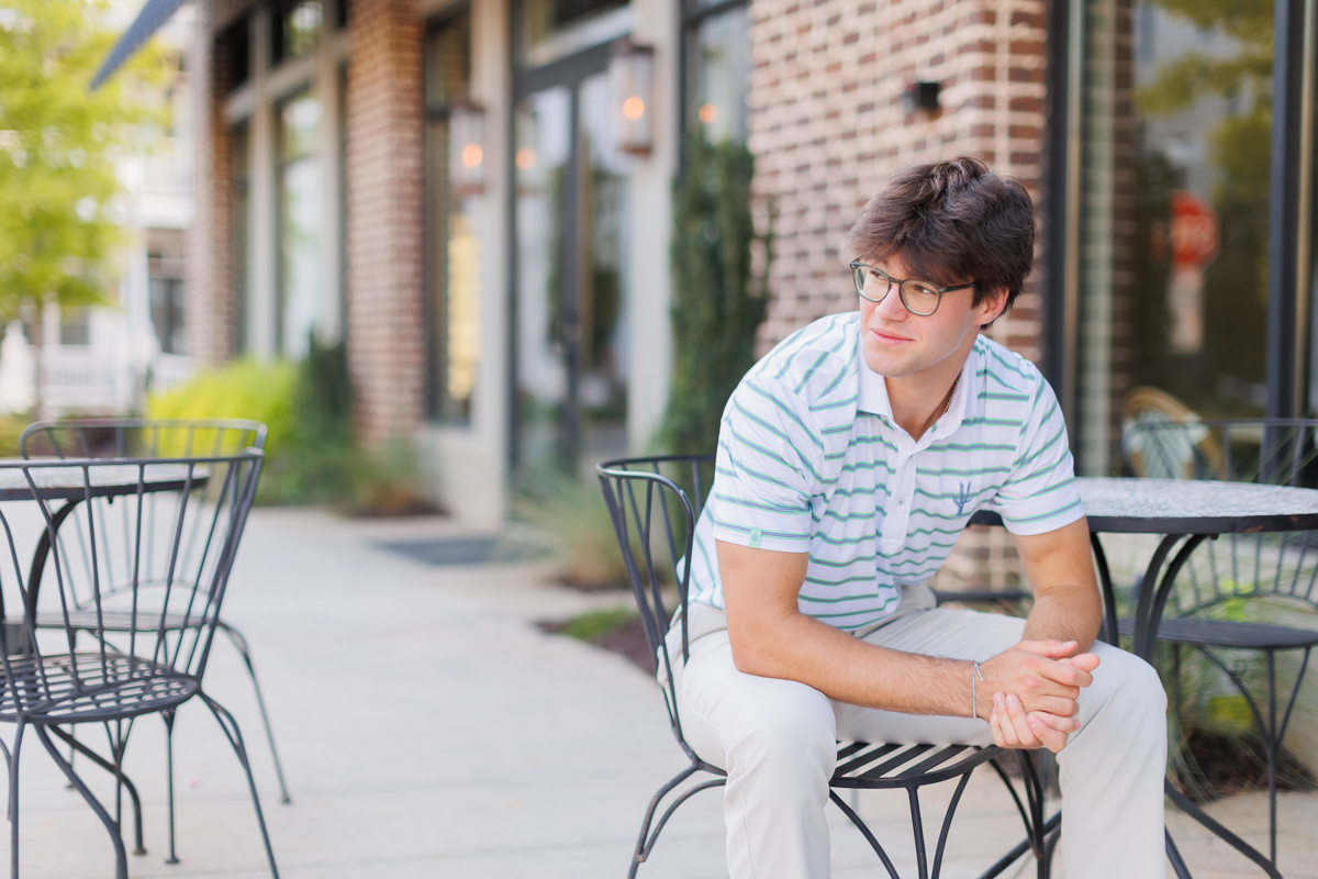 High school senior boy sits on metal chair outside cafe in Woodstock, Georgia